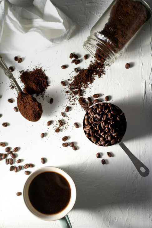 Image of a cup of coffee surrounded by coffee beans and ground coffee.